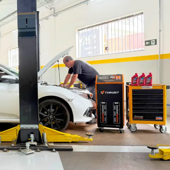 Técnico da Pneuscarmg trabalha no cofre de um Honda Civic branco, ao lado do trocador de fluido ATF Thrust e de frascos de fluido Valvoline