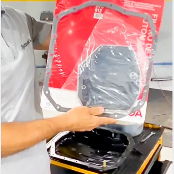 Técnico segura o kit de filtro e junta do câmbio automático, ainda na embalagem, acima do cárter removido