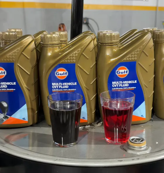 Frascos de fluido para câmbio CVT e dois copos lado a lado: fluido usado escuro e fluido novo vermelho
